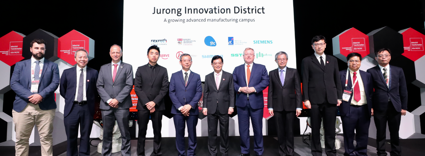 Group of people in suits on a stage in front of a screen about Jurong Innovation District.